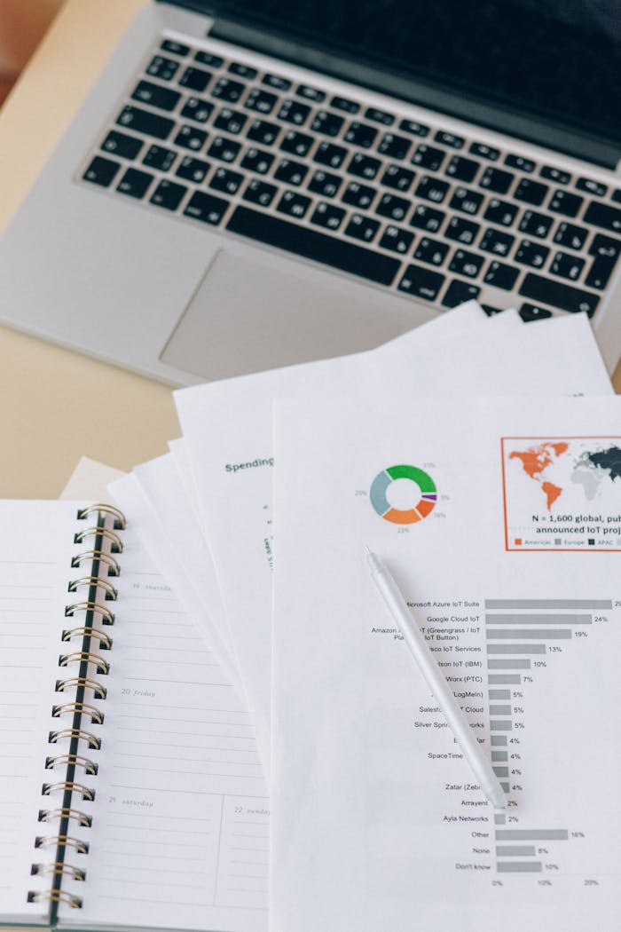 Close-up of a workspace with a laptop, notebook, and financial reports, ideal for business contexts.